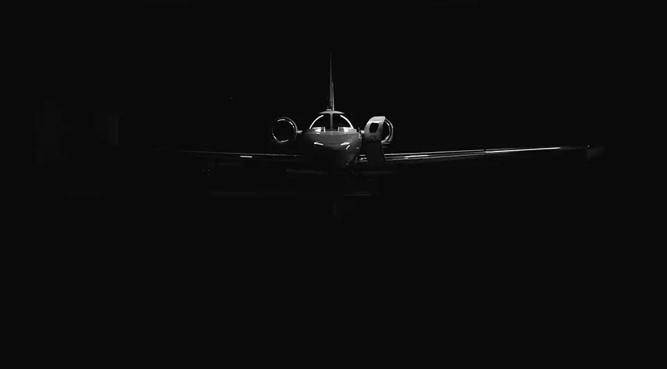 A private jet in a dark hangar, rim-lit, its door open