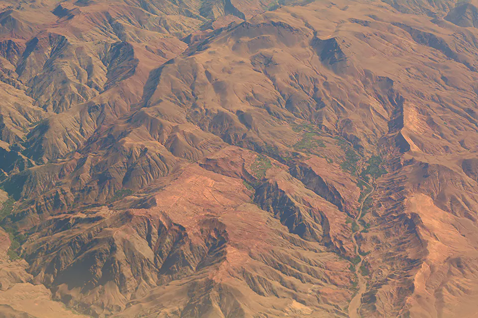 Folded terracotta mountains and green valleys in Morocco, seen from the air