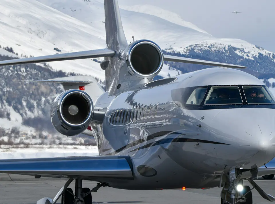 A three-engine large-cabin business jet on an apron below snowy mountains