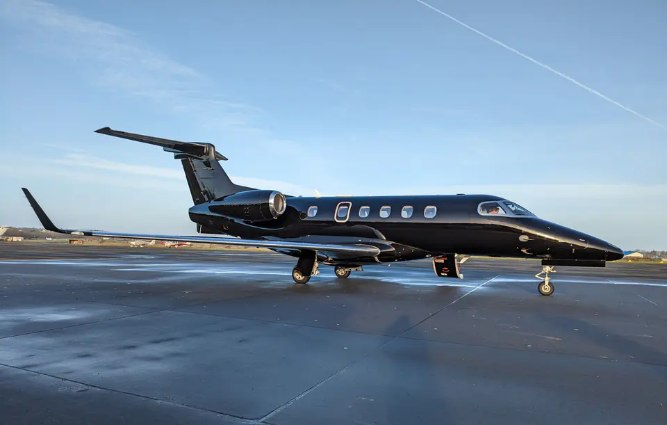 A black Embraer Phenom 300 light jet on a wet apron