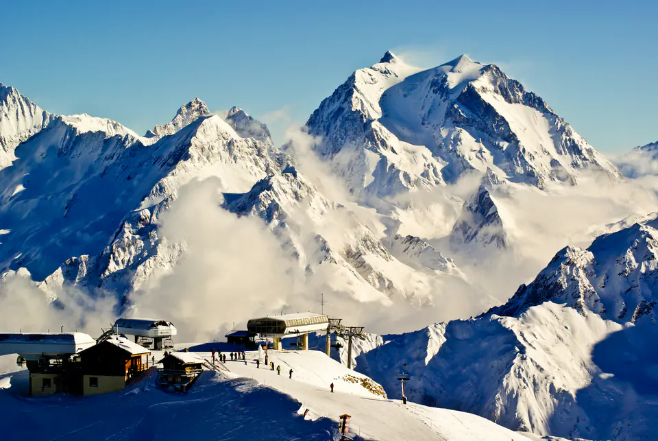 A snow-covered peak rising above the clouds at Courchevel, a lift station in the foreground