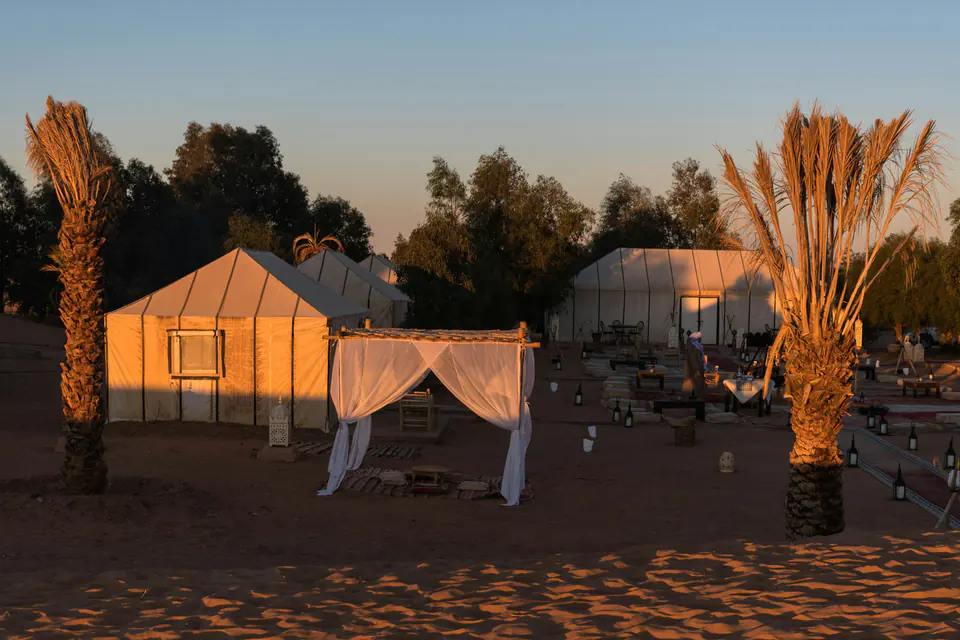 Tents, palms and lanterns of a desert camp at Erg Chebbi in the last light