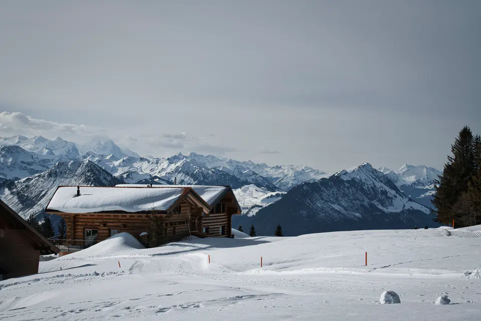A log chalet in deep snow above Gstaad, a range of peaks beyond