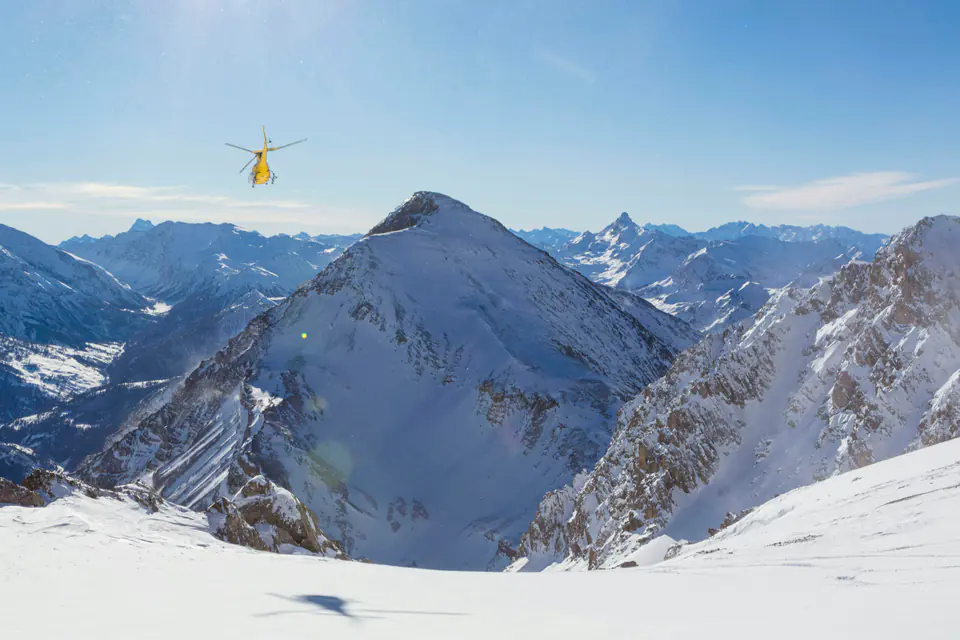 A yellow helicopter flying toward a snow-covered peak in the French Alps