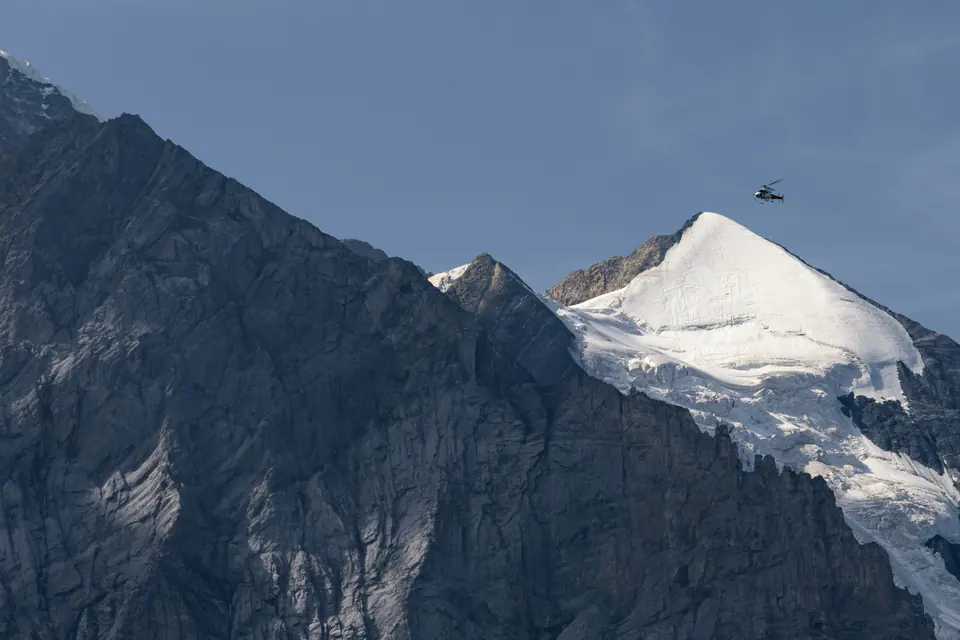 A helicopter flying past a snow-covered summit at the Jungfraujoch in the Swiss Alps