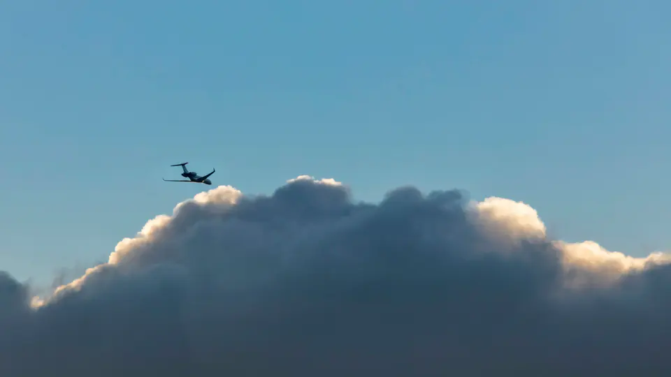 A private jet climbing above a sunlit bank of cloud