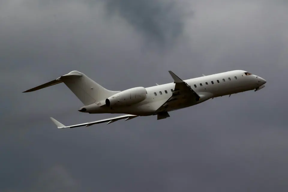 A white long-range business jet climbing through a grey storm sky