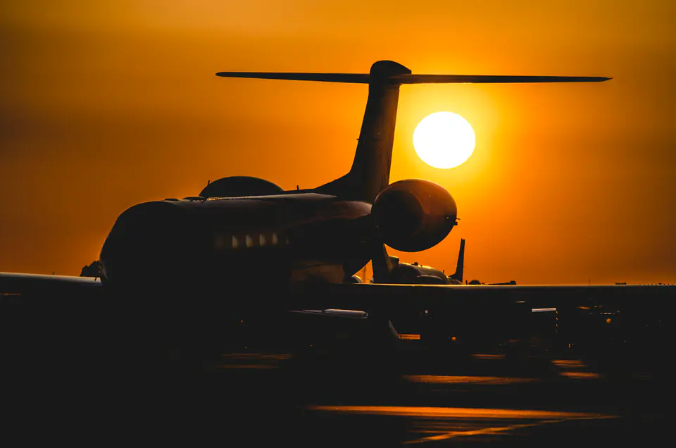The tail and engine of a private jet in silhouette against the setting sun