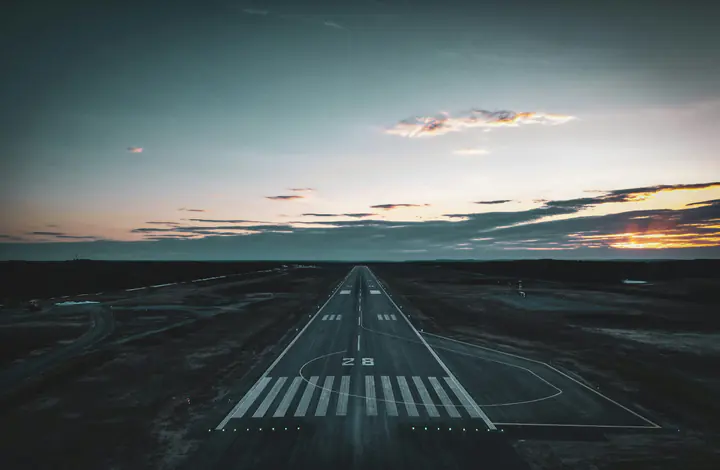 A runway seen from above at dusk, its lights leading to the horizon