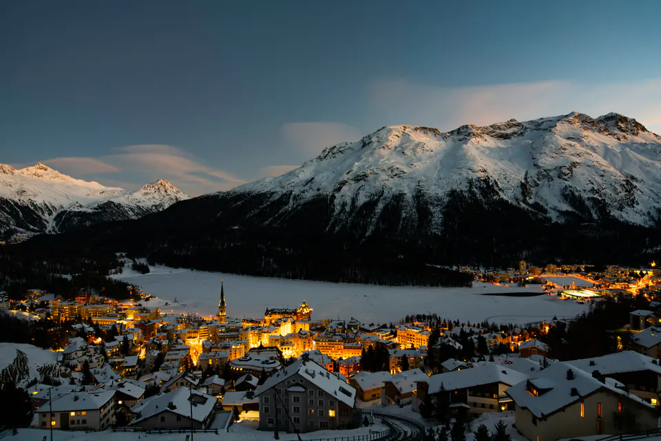 St. Moritz at dusk, its lights along the frozen lake below snowy peaks