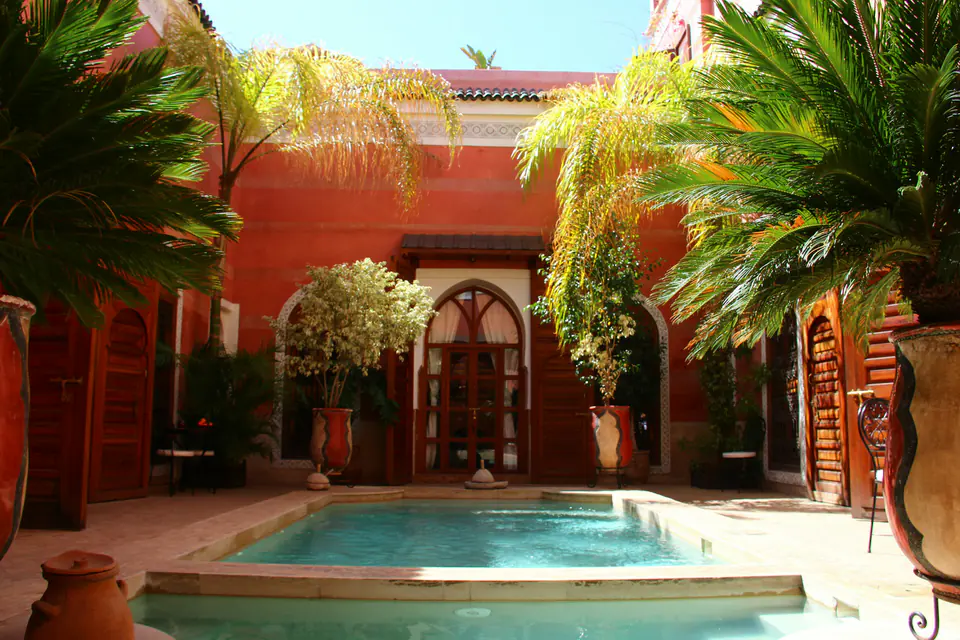 A swimming pool in a red-walled garden courtyard in Marrakech