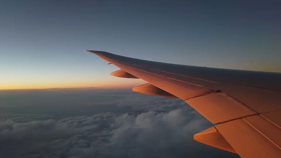 An aircraft wing glowing copper above the clouds at sunset, seen from a cabin window