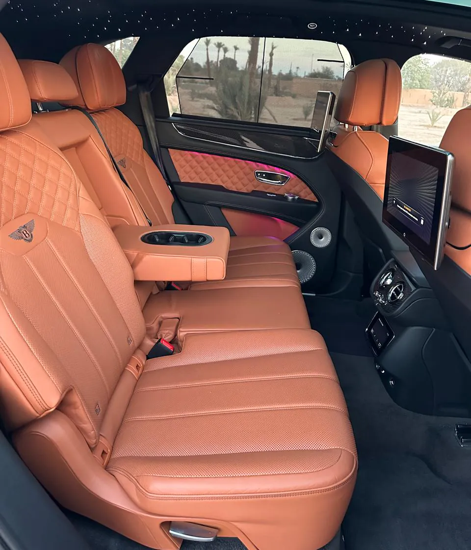 Rear seats of the Bentley Bentayga in tan leather, with the centre armrest folded down