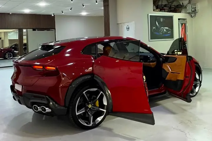 Red Ferrari Purosangue with its rear-hinged back doors open, showing the tan cabin