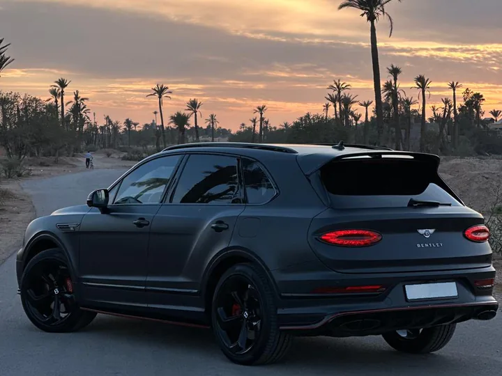 Matt grey Bentley Bentayga from the rear three-quarter, on a palm-lined road at sunset